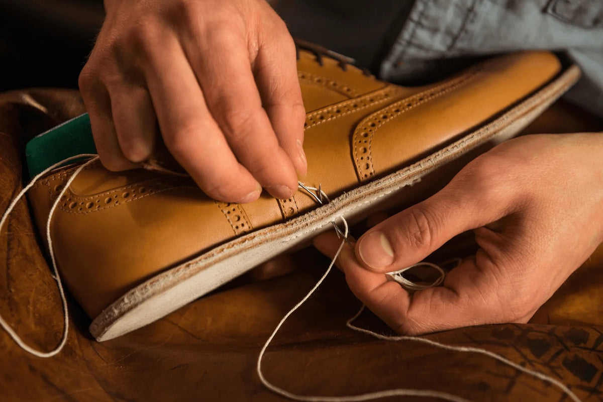 Hands hand-stitching the welt of a tan leather brogue